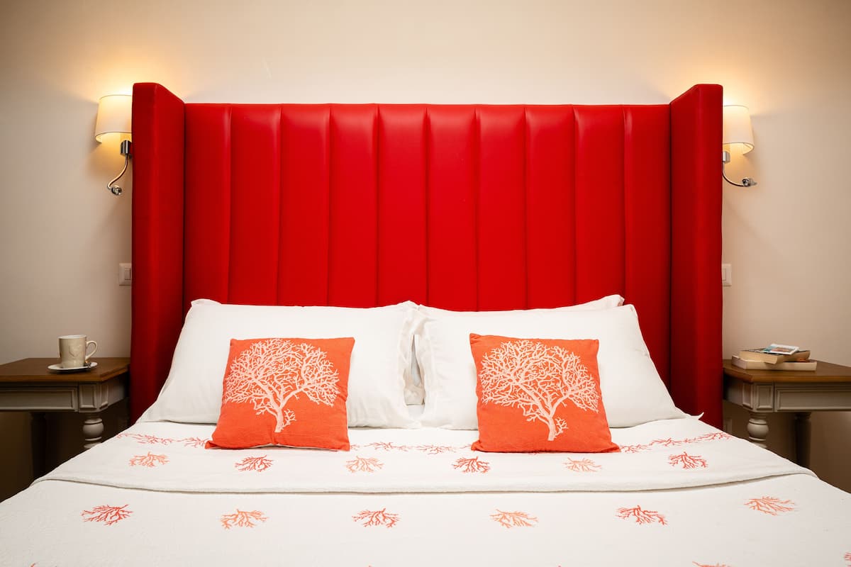 Une chambre d’hôtel avec une tête de lit rouge, du linge de lit blanc et deux tables de chevet avec des lampes.