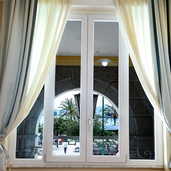 A window with white frames and a view of a street with palm trees and parked cars.