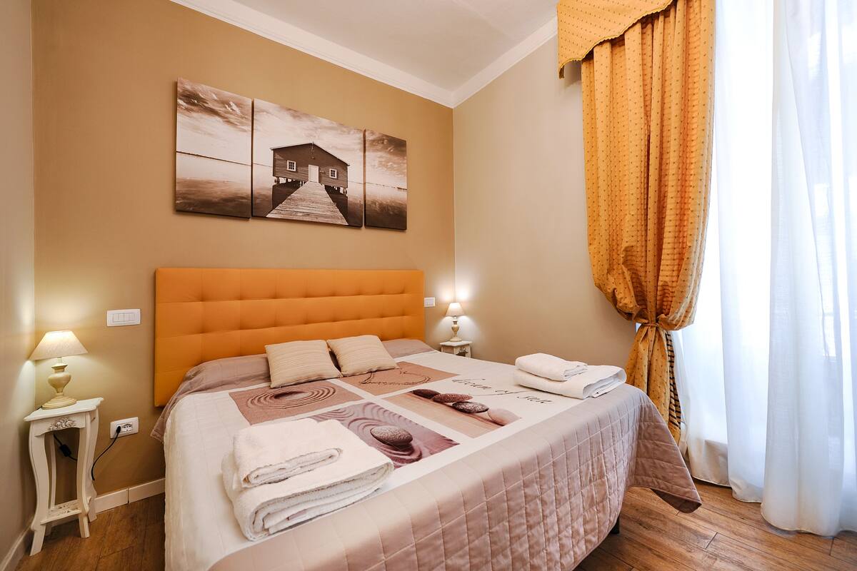 Un lit bien fait, avec une tête de lit matelassée, une table de chevet avec une lampe et un tableau au-dessus du lit.