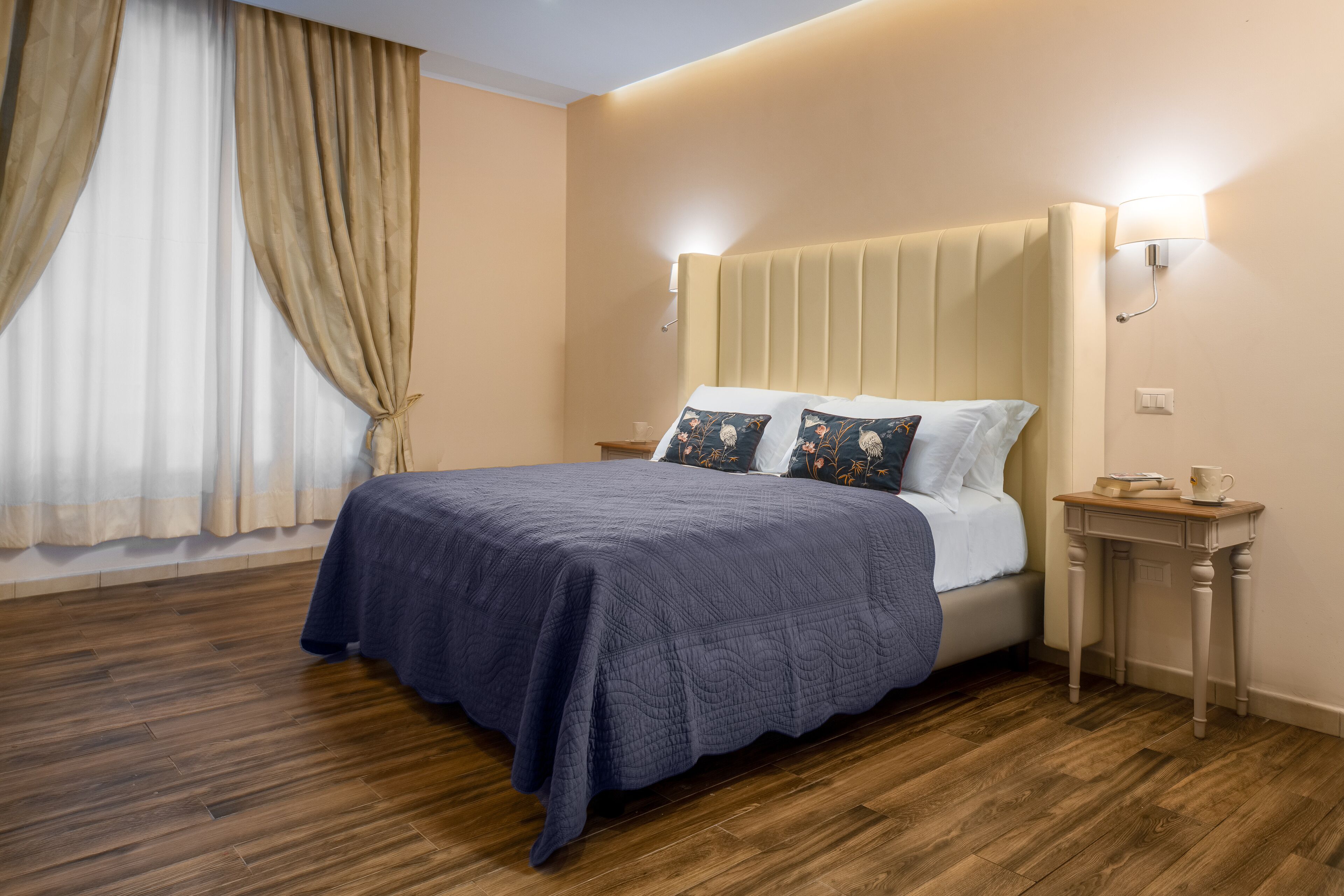 A neatly made bed with a blue bedspread, two pillows, and a bedside table with a lamp.