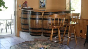 Un coin bar avec des tonneaux en bois, une table carrelée et un tableau encadré au mur.