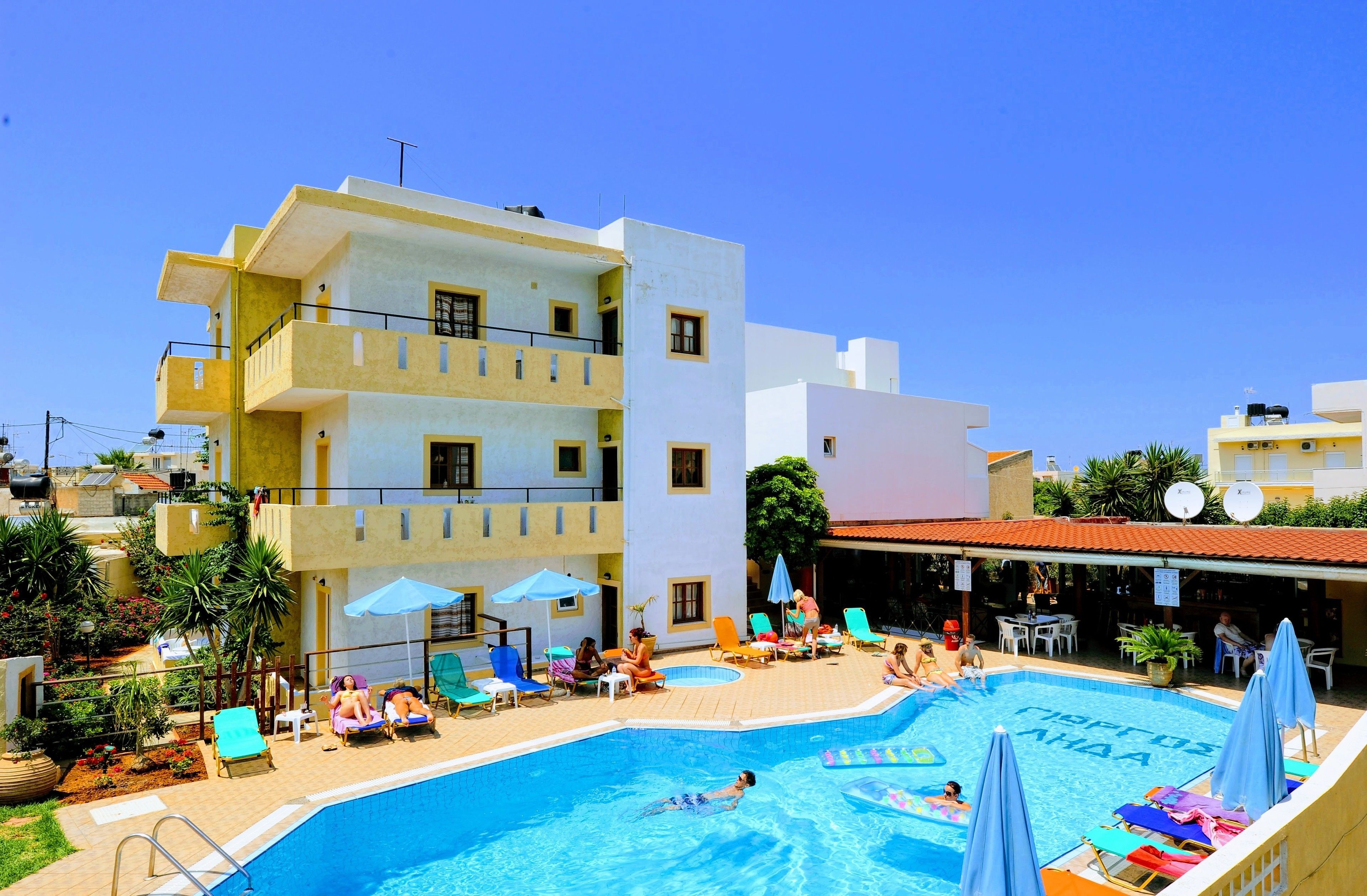 A swimming pool area with lounge chairs and umbrellas, surrounded by multi-story buildings.