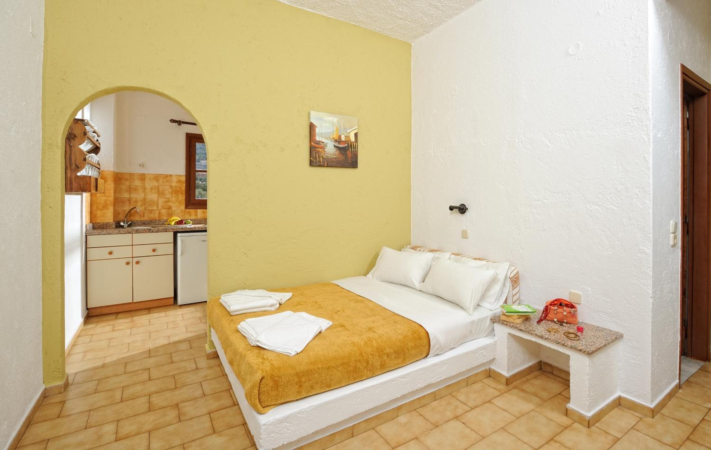 A bedroom with a bed, a bedside table, and a view of a kitchen.