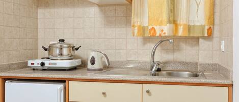 A compact kitchen with a refrigerator, stove, sink, and a dining table with a fruit plate.