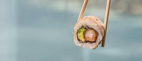 A sushi roll being held by chopsticks, with a pool view in the background.