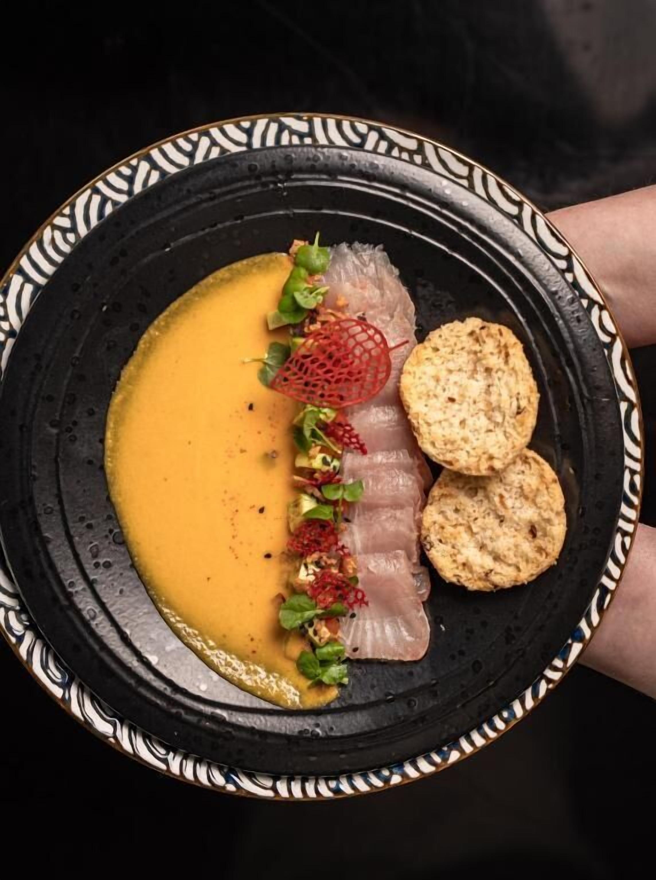 A plate with a creamy soup, thinly sliced meat, and crackers.