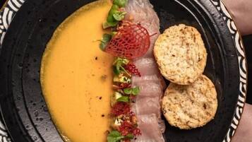A plate with a creamy soup, thinly sliced meat, and crackers.