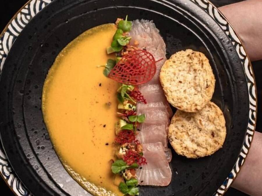 A plate with a creamy soup, thinly sliced meat, and crackers.