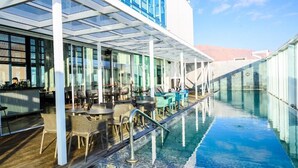 Uma área à beira da piscina com assentos externos, bar e piscina envidraçada.
