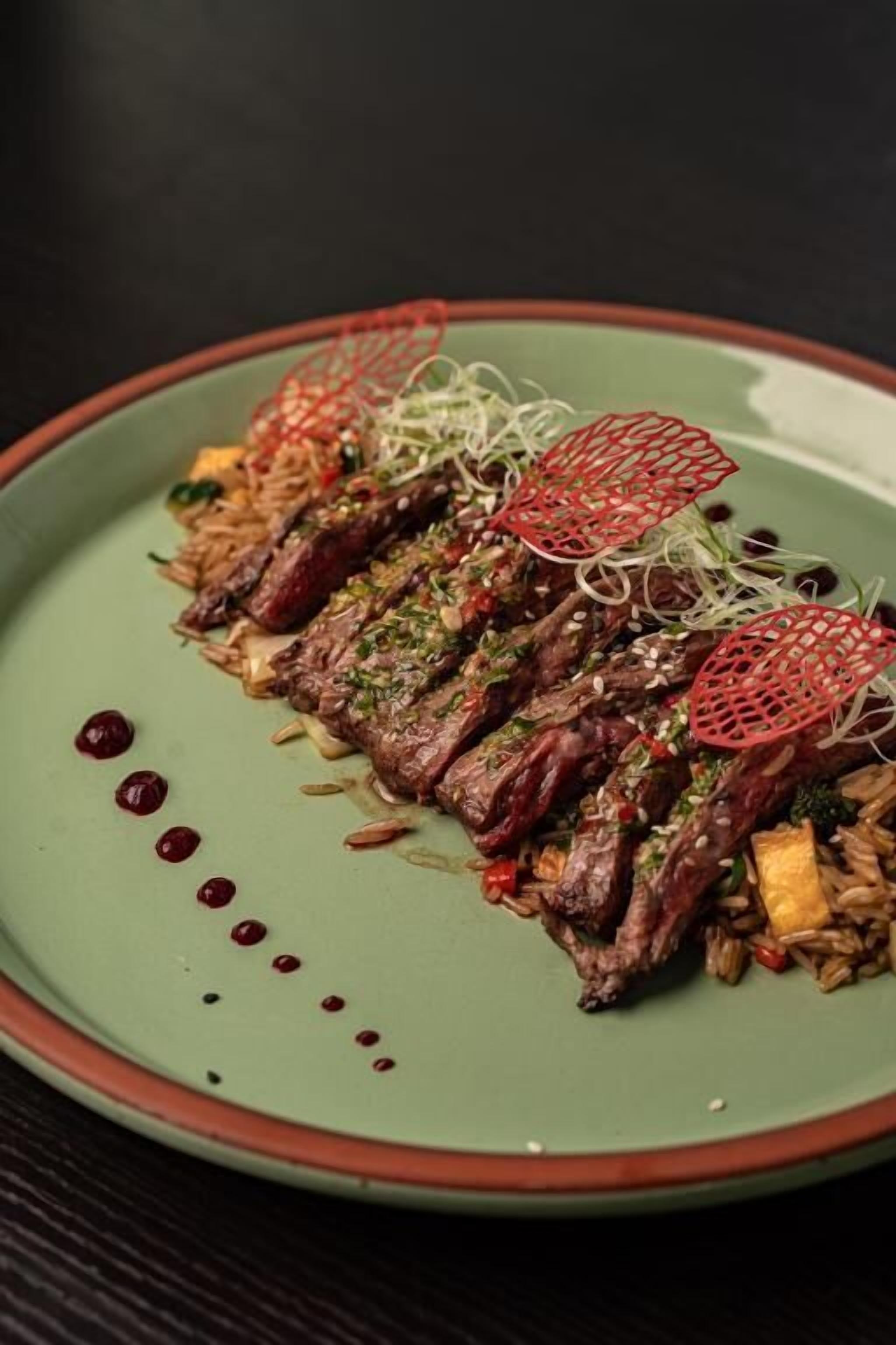 A plate of food with a green rim, containing sliced meat, rice, and garnishes.