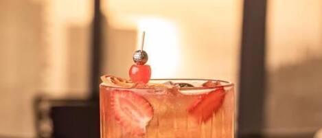 A hand holding a cocktail glass with a strawberry garnish, set against a blurred indoor background.