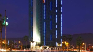 Um hotel alto com fachada de vidro moderna e o nome 'TERRADO' iluminado na lateral.
