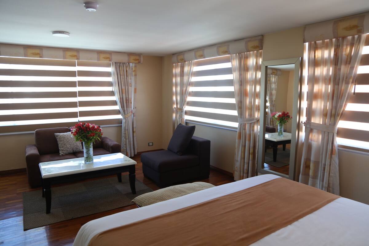 A hotel room with a bed, a sofa, a coffee table, and a mirror.