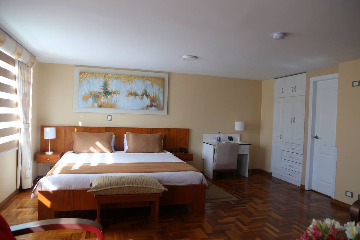 A bedroom with a bed, bedside table, desk, wardrobe, and a painting on the wall.