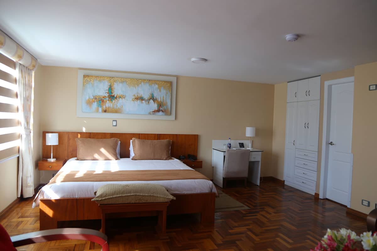 Um quarto com cama, mesa de cabeceira, escrivaninha, guarda-roupa e um quadro na parede.