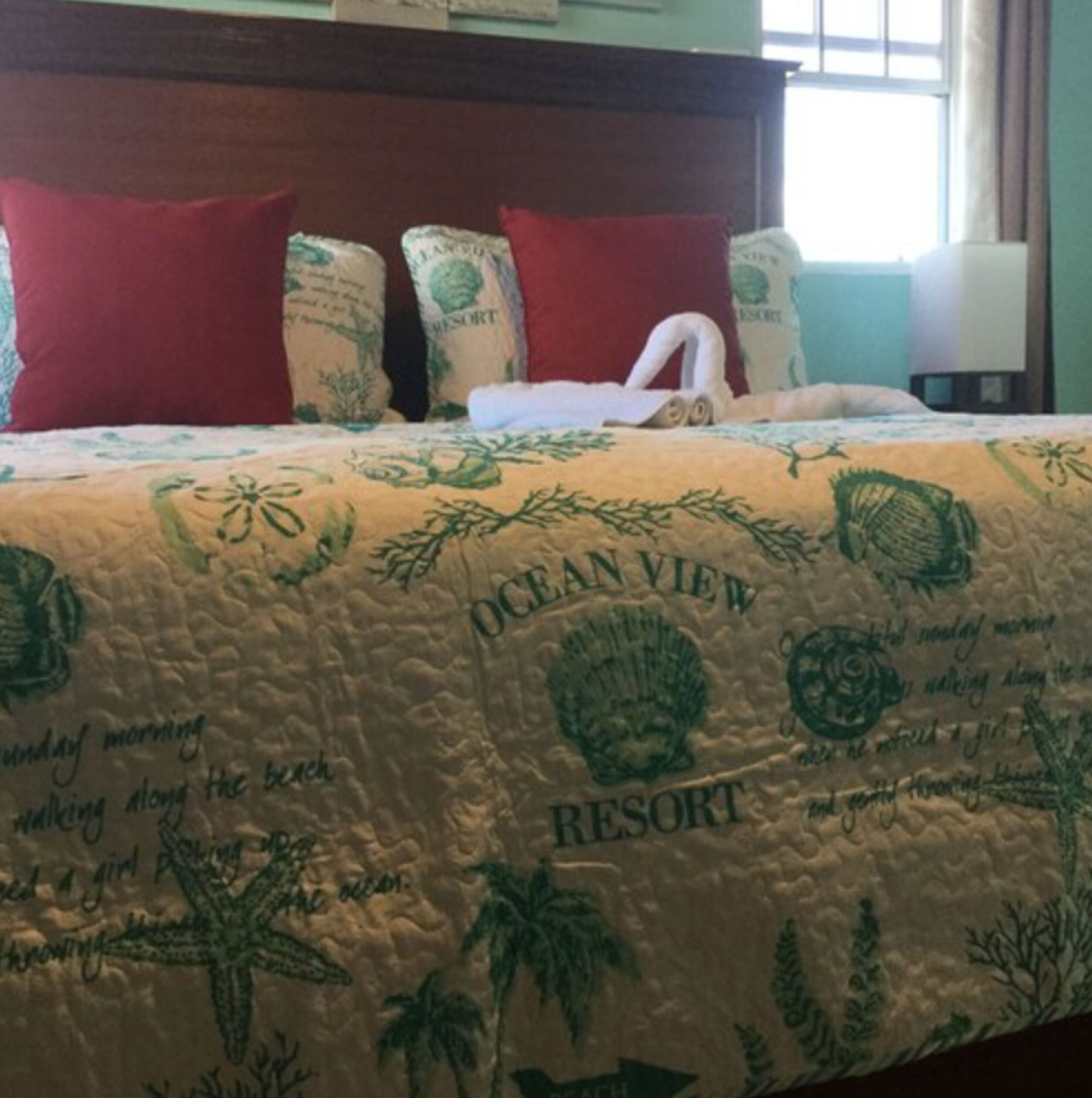 A bed with a quilt featuring ocean and beach motifs, red pillows, and a white towel.