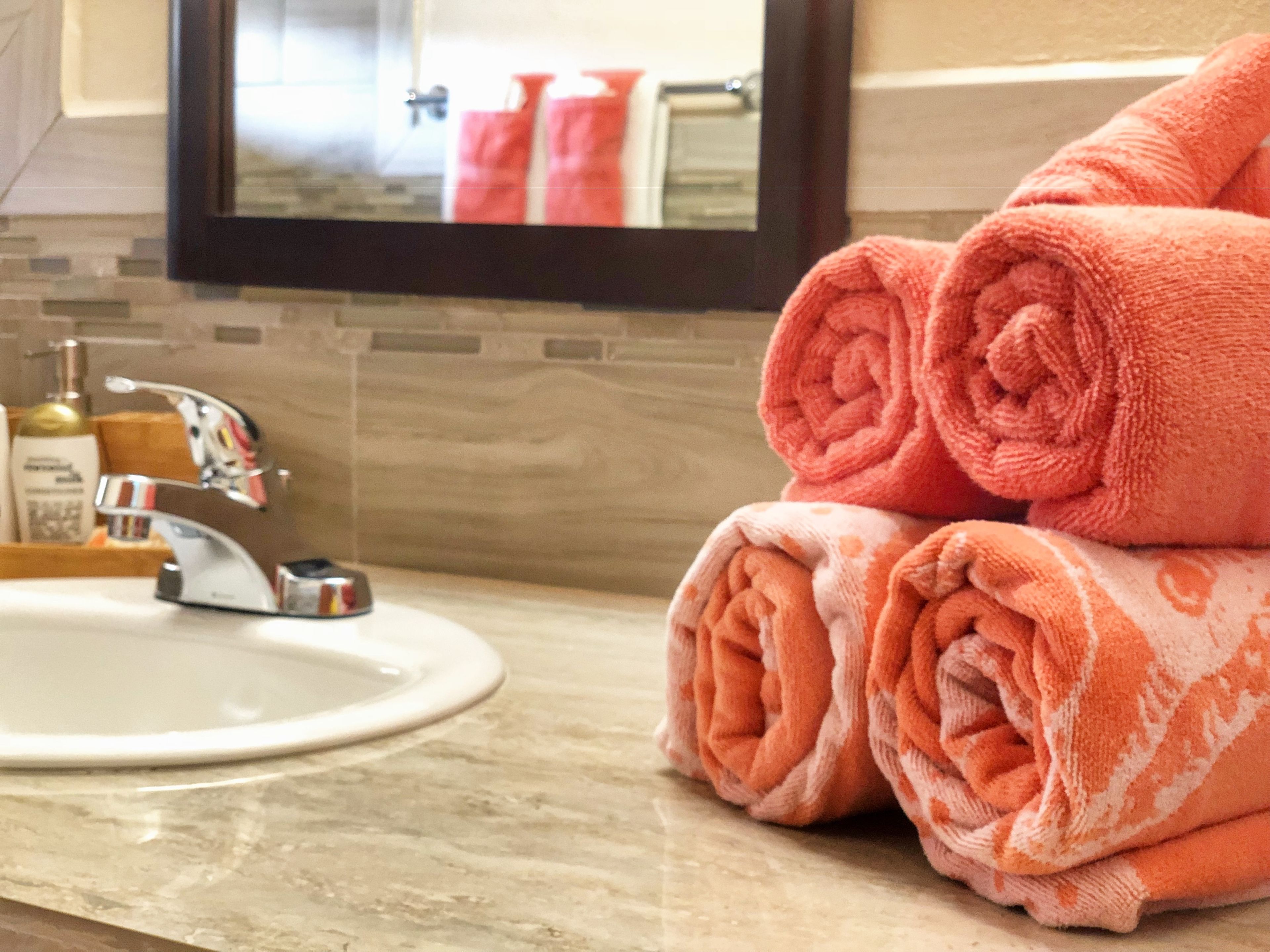 A bathroom with a sink, a mirror, and a towel rack with rolled towels.