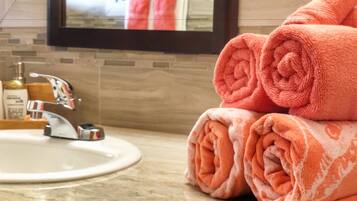 A bathroom with a sink, a mirror, and a towel rack with rolled towels.