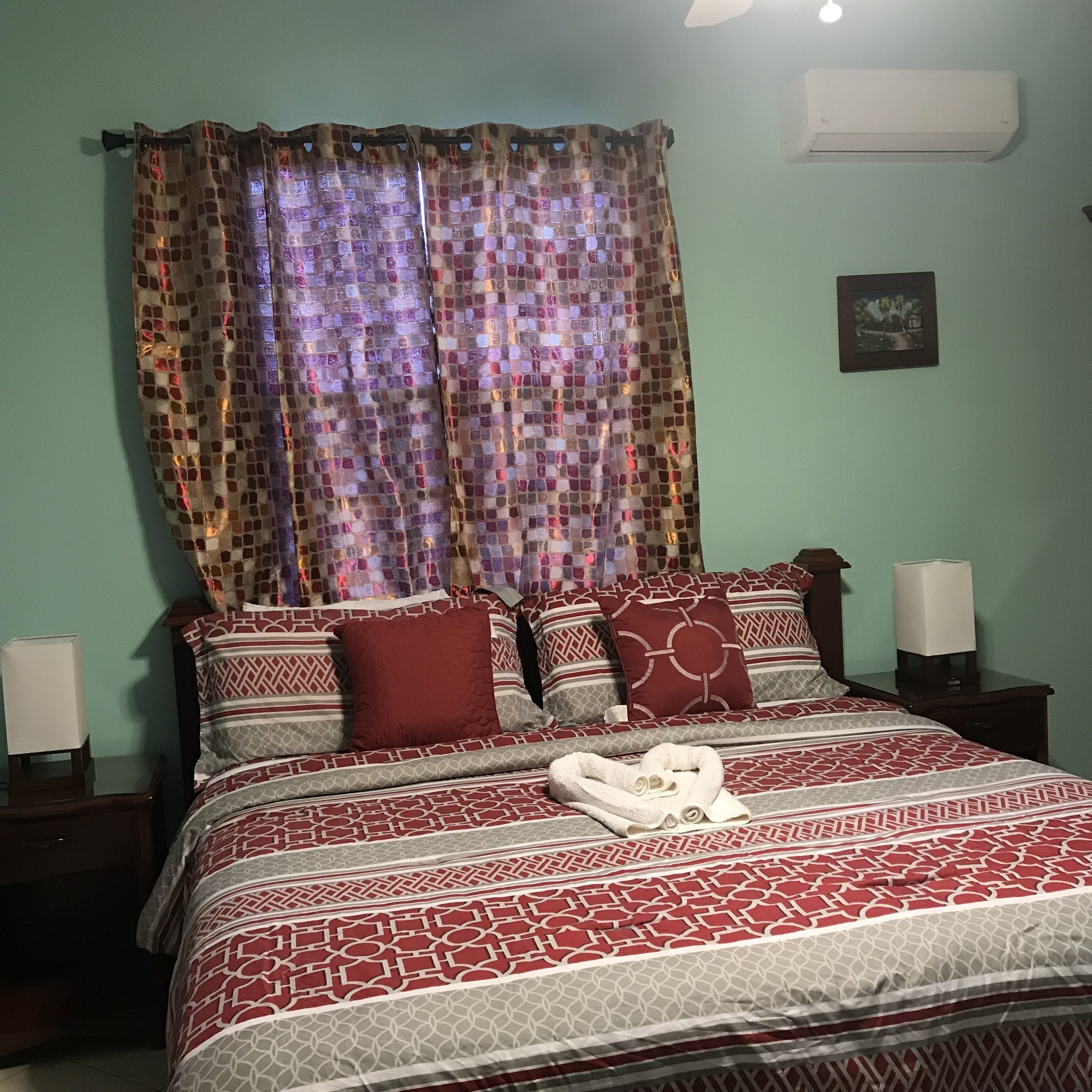 Un letto rifatto con cura, lenzuola a motivi decorativi, una tenda ornamentale e un quadro appeso al muro.