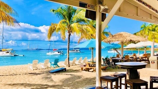Blick auf einen Strand mit Liegestühlen, einem Tisch und Sonnenschirmen.