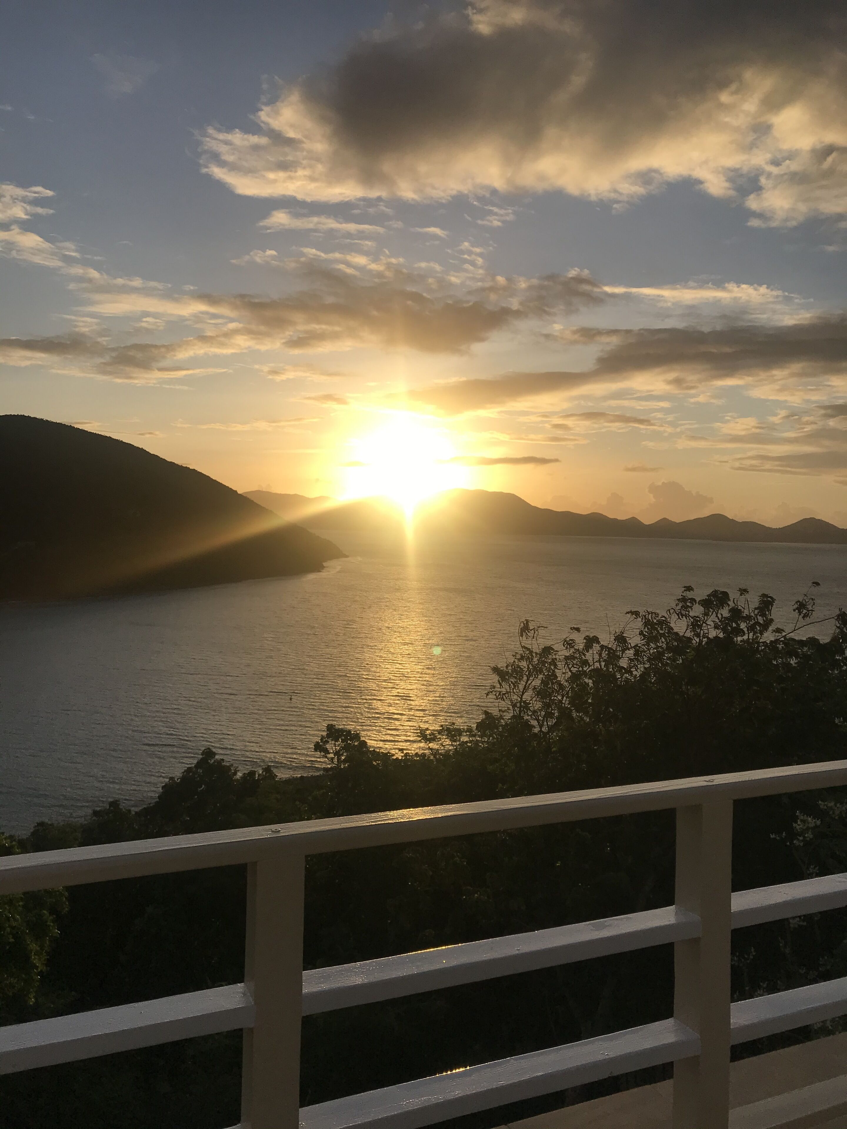Una puesta de sol sobre un cuerpo de agua con montañas al fondo.