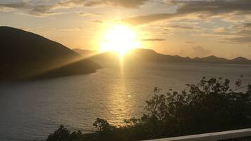 Una puesta de sol sobre un cuerpo de agua con montañas al fondo.