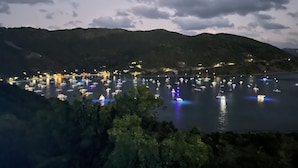 Eine Küstenstadt bei Nacht mit in der Bucht liegenden Booten, umgeben von Hügeln.