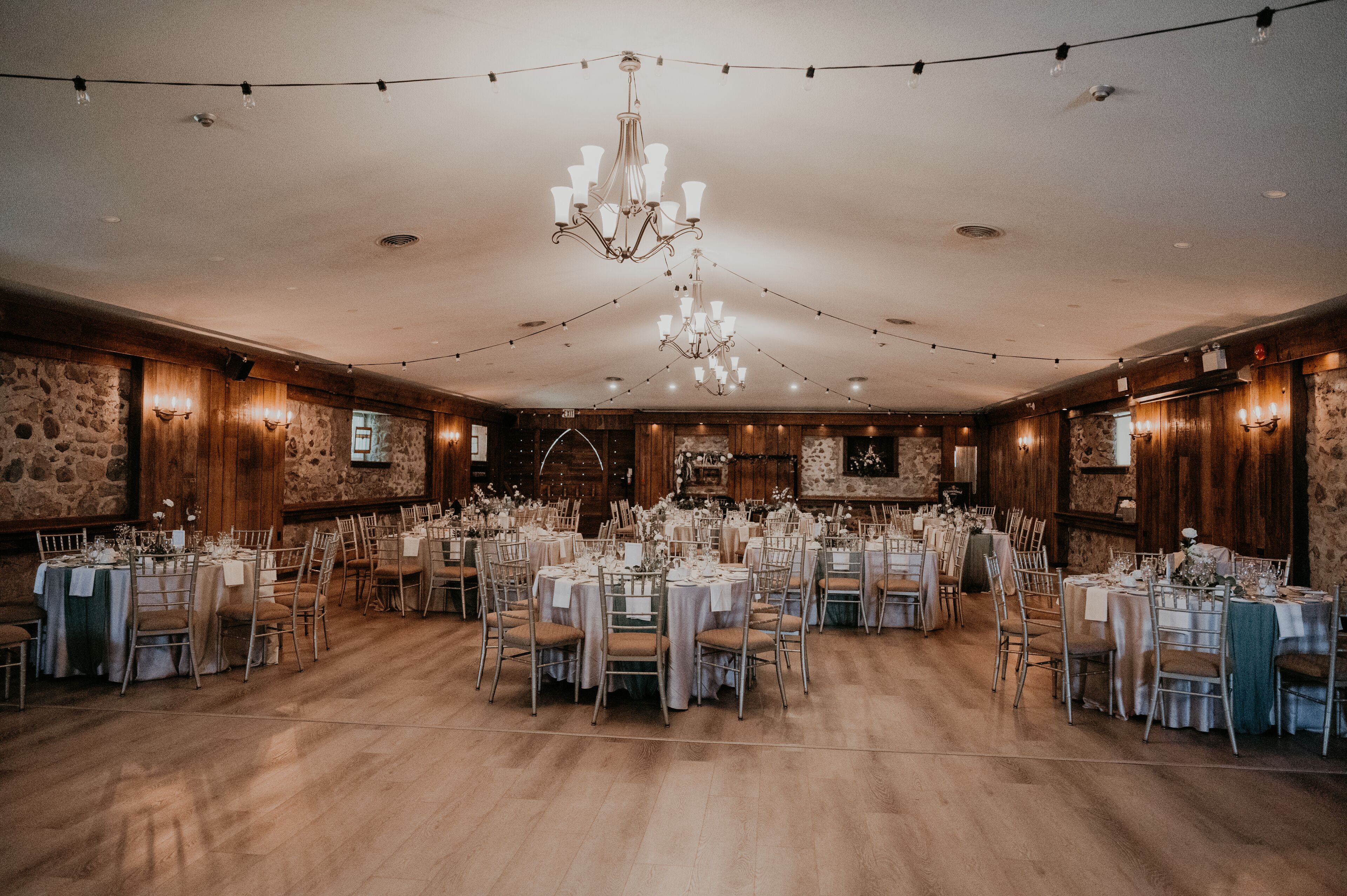 A banquet hall with multiple round tables, wooden walls, and a chandelier.