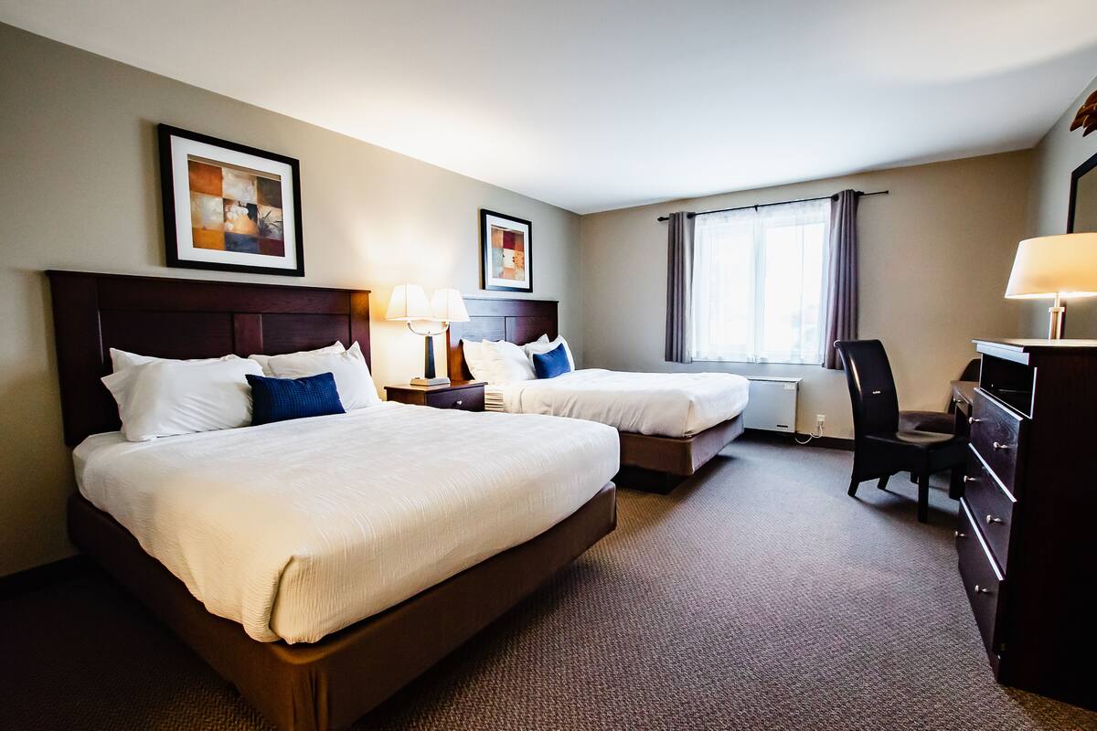 A hotel room with two beds, a desk, a chair, and a window with curtains.