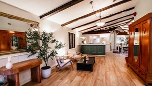 A spacious living room with wooden floors, a large wooden cabinet, a dining area with a green table, and a kitchen in the background. - Hessenland Inn & Schatz Winery (Bluewater)