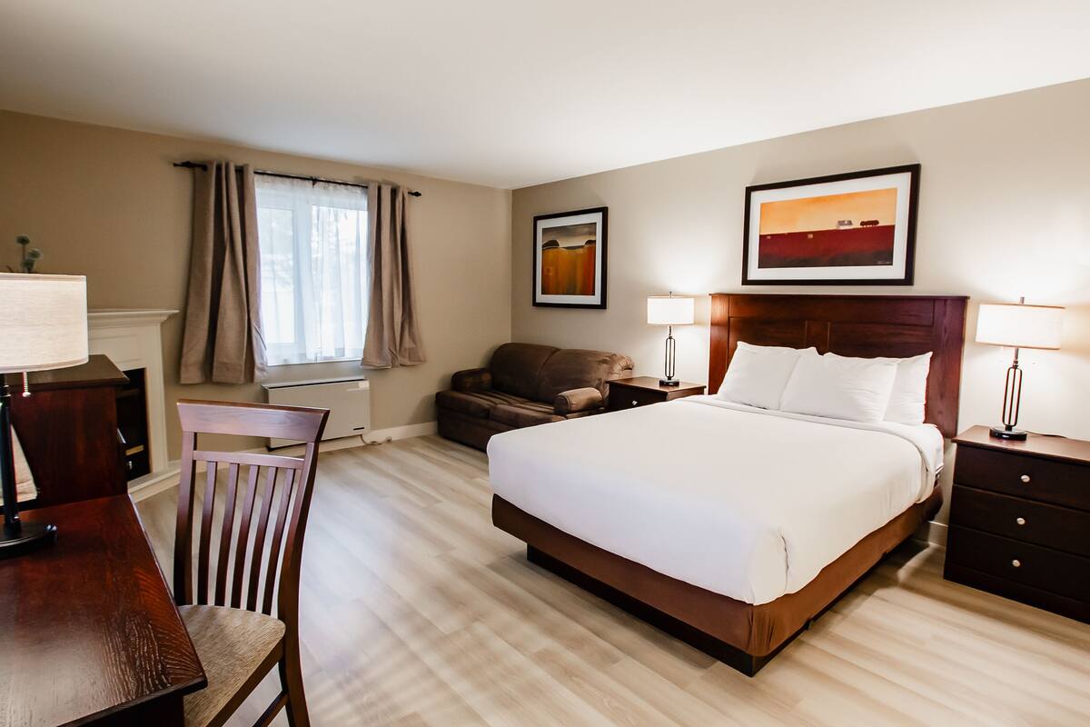 A hotel room with a large bed, a desk, a chair, a sofa, and two lamps.