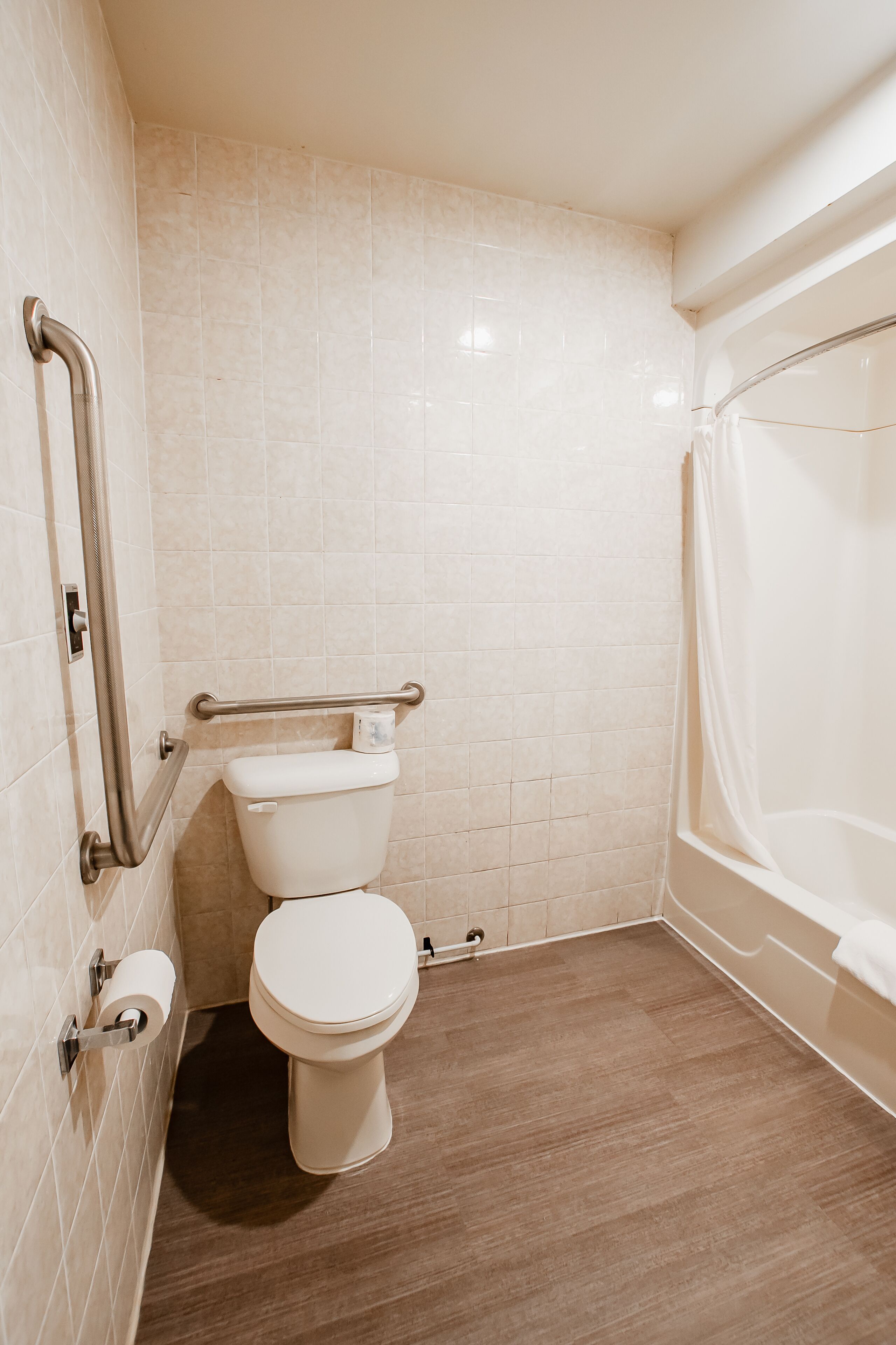 Ein Badezimmer mit Toilette, Haltegriffen, einer Duschvorhang und einer Toilettenpapierrolle.