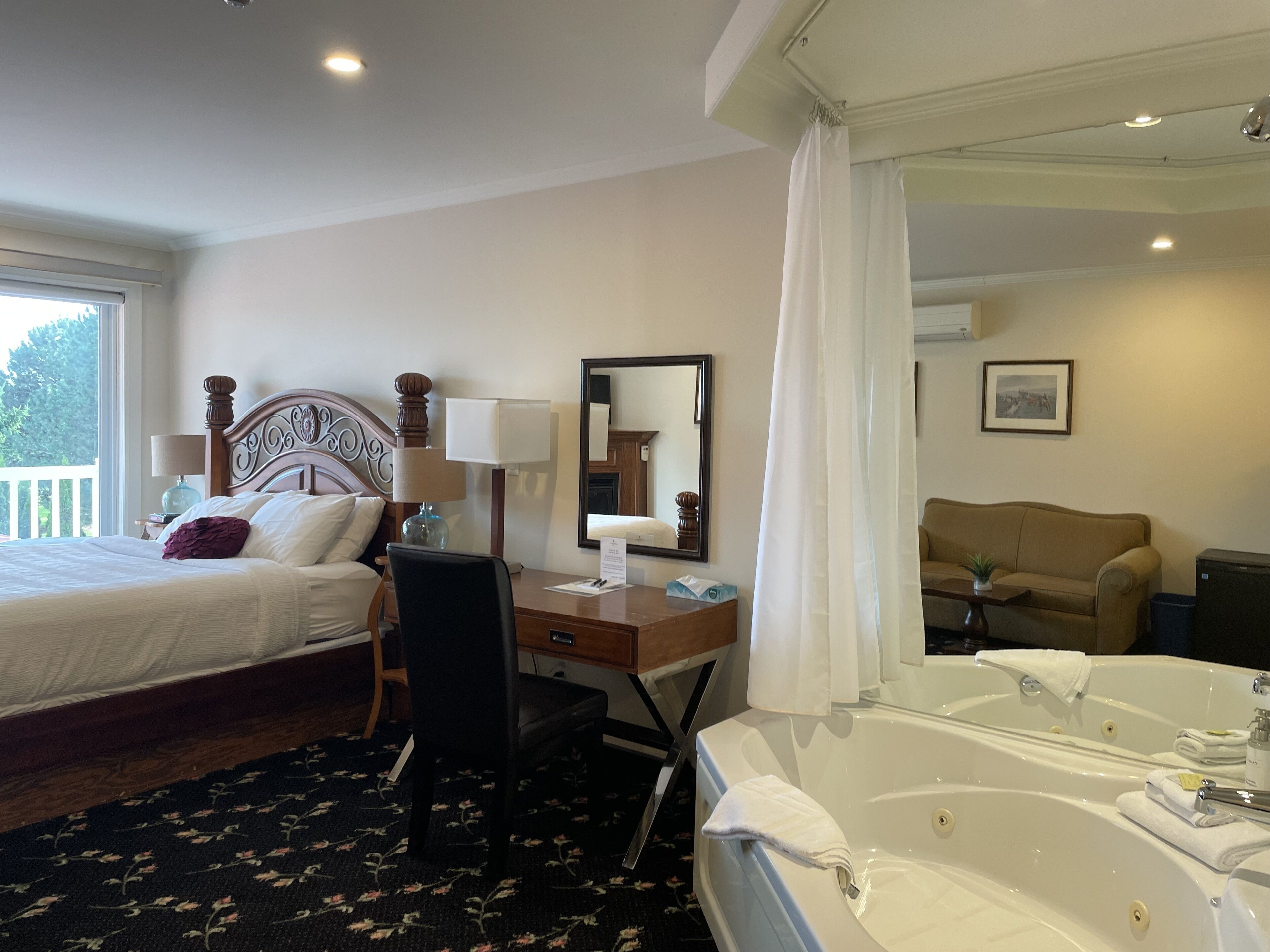 A hotel room with a bed, desk, chair, and a large bathtub.