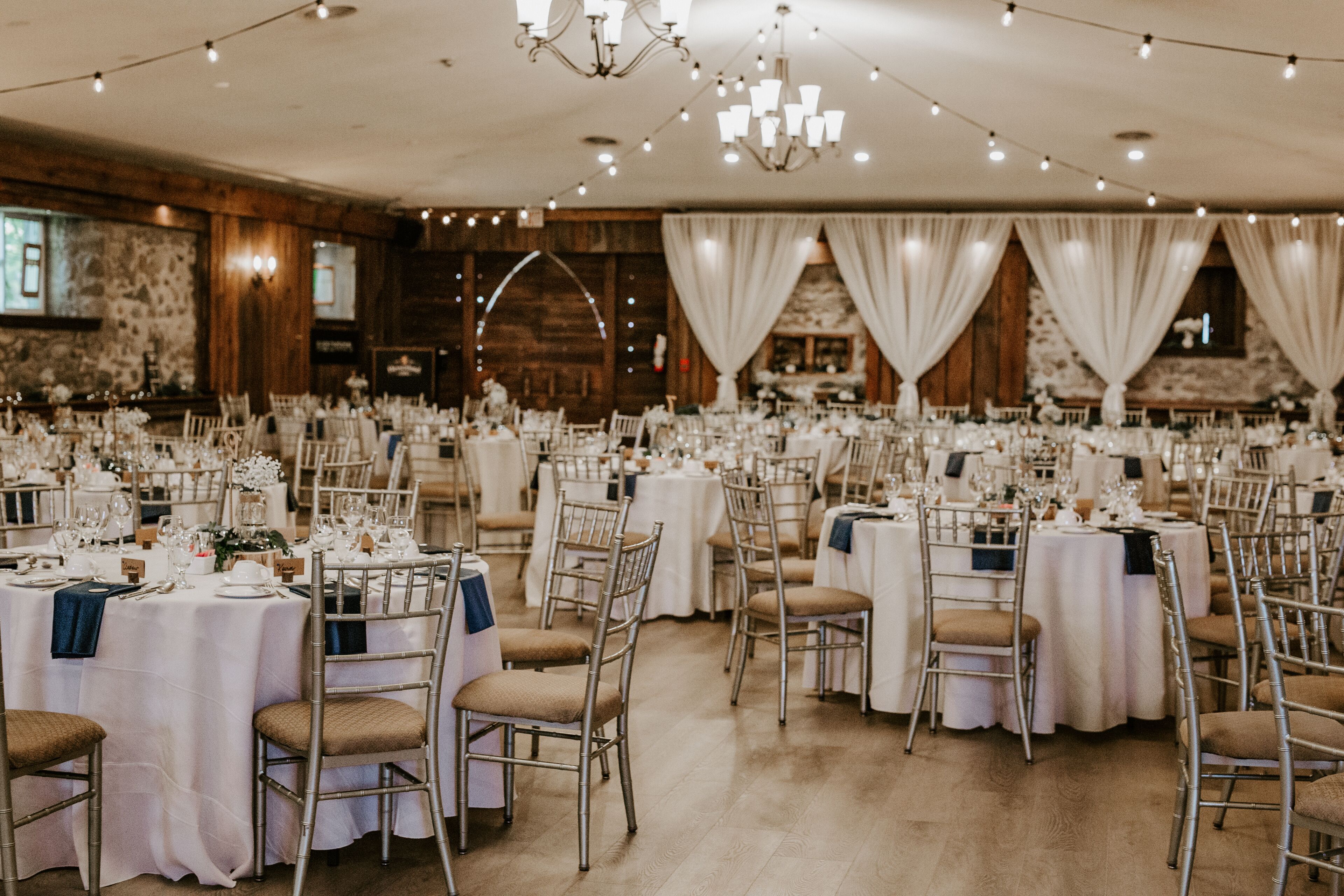 Un salón de banquetes con mesas redondas dispuestas para un evento formal, con manteles blancos y sillas doradas.