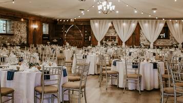 Un salón de banquetes con mesas redondas dispuestas para un evento formal, con manteles blancos y sillas doradas.