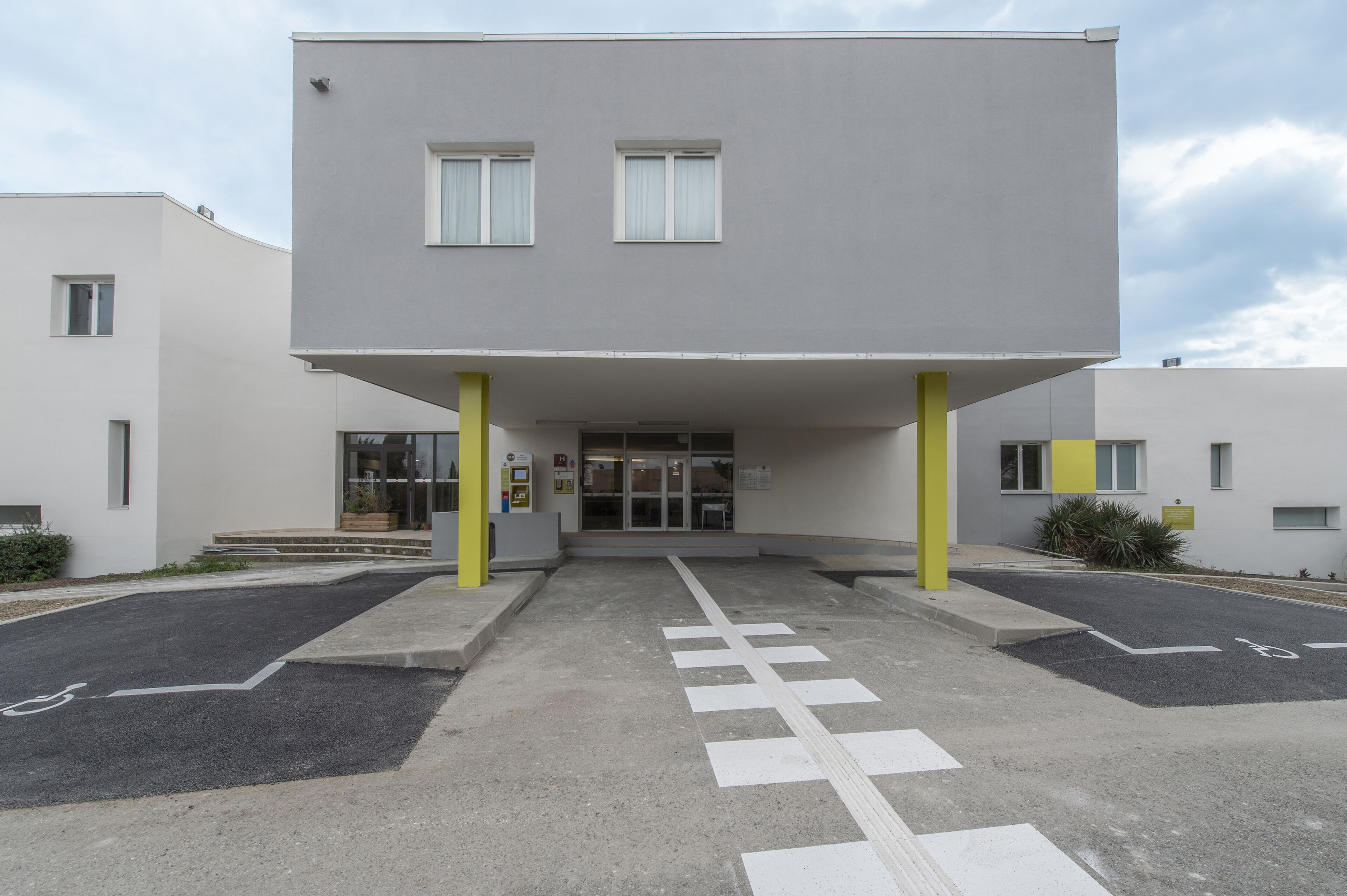 A modern building with a flat roof, two visible windows, and a yellow pillar.