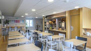 Una cafetería con varias mesas y sillas, una barra con alimentos y una zona de estar con plantas.