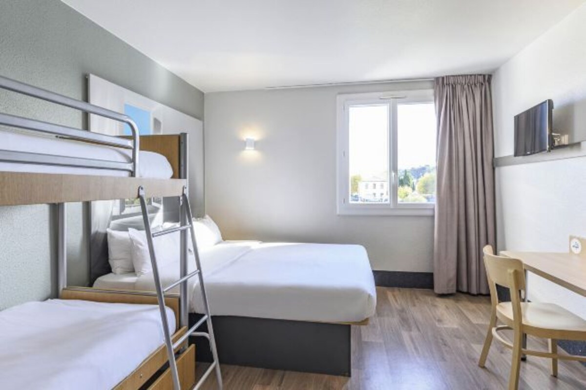 A hotel room with two beds, a desk, a chair, a TV, and a window with curtains.