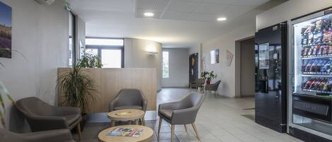 A modern lobby with seating, a vending machine, and a reception desk.