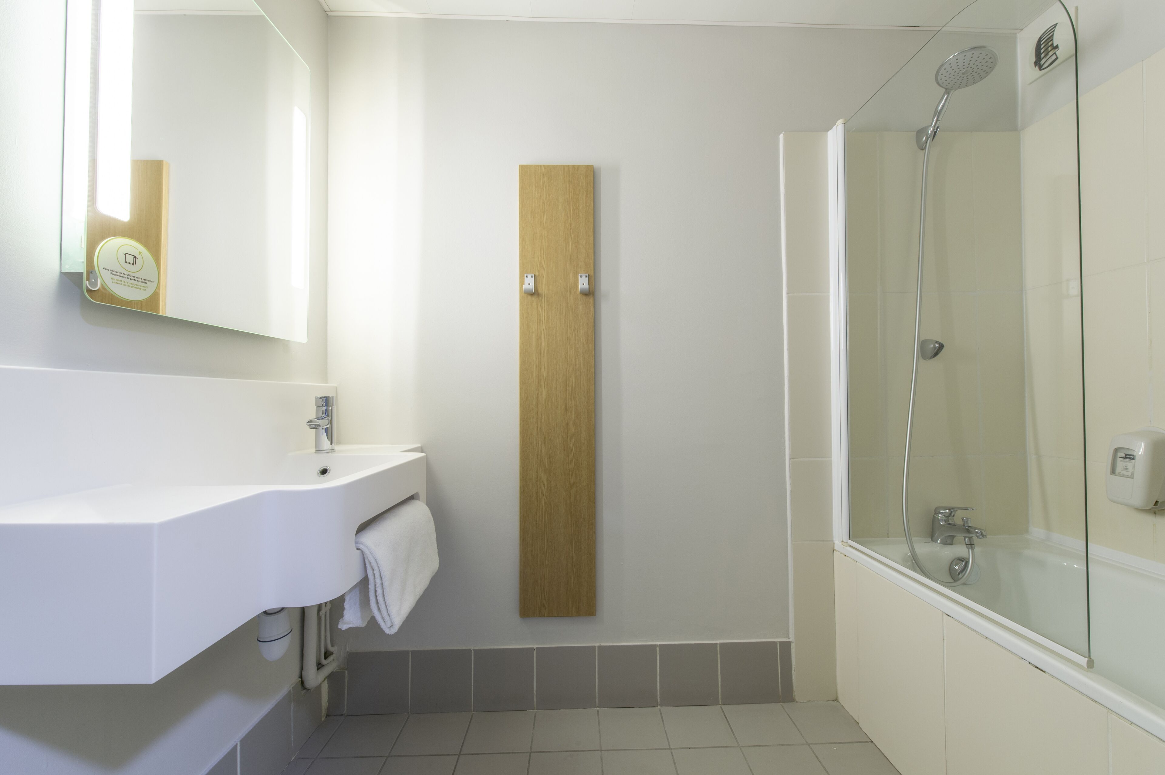 Un baño moderno con un lavamanos blanco, panel de madera y ducha con cerramiento de vidrio.