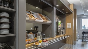 A modern breakfast bar with a variety of food items and beverages, including pastries, fruits, and coffee. - B&B HOTEL Orange (Orange)