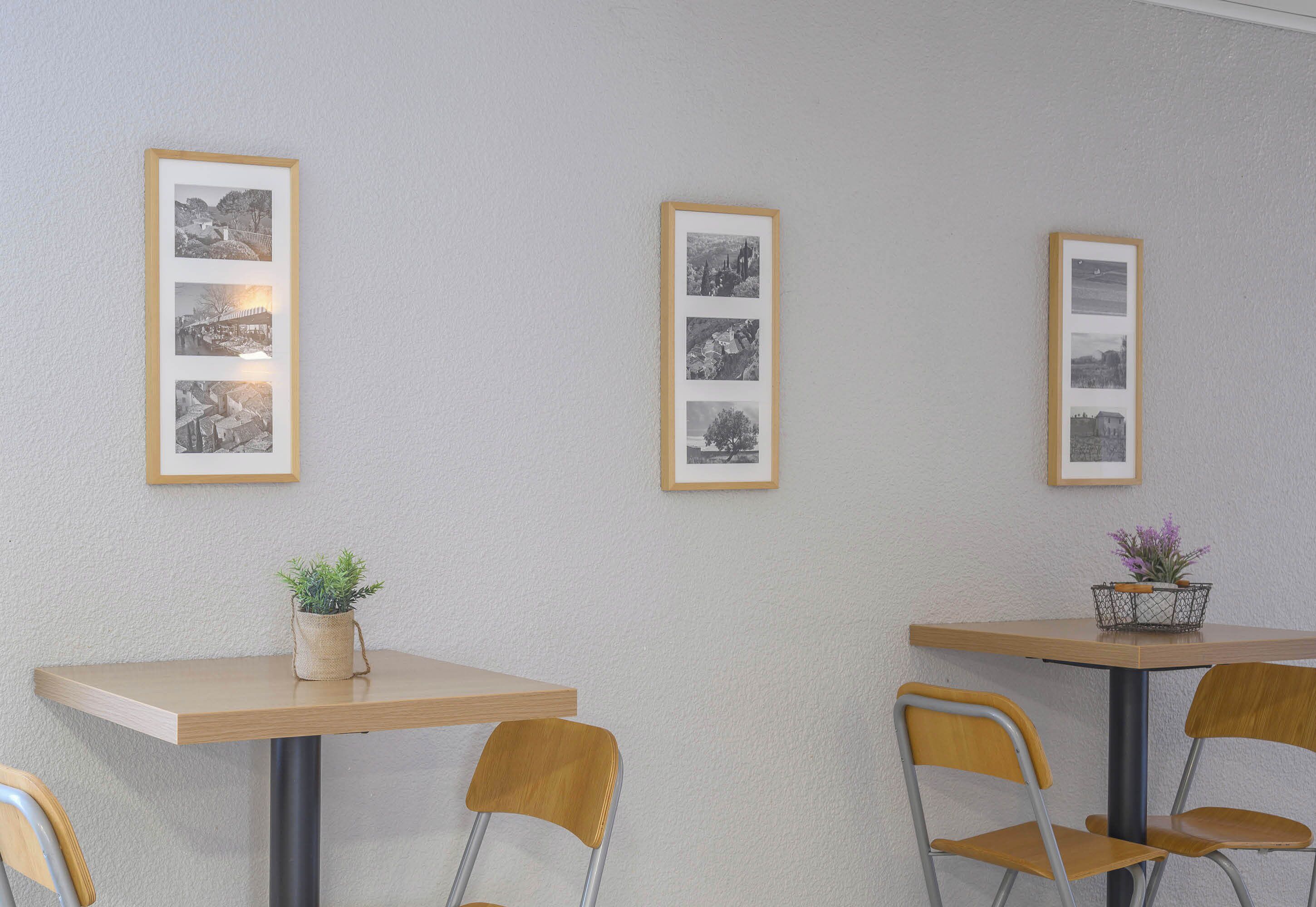 Comedor con dos mesas, cada una con un collage de fotos enmarcadas en la pared superior. Hay dos sillas en cada mesa, y una planta pequeña en la mesa de la izquierda.