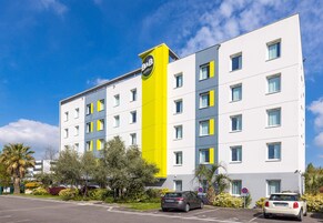 Un hôtel moderne, avec une façade jaune et blanche bien visible, de nombreuses fenêtres et un parking où sont garées des voitures.