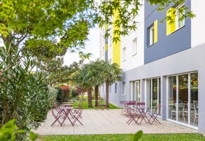 Une cour dotée d’un espace extérieur aménagé, entourée de verdure et bordée d’un bâtiment moderne aux grandes fenêtres.