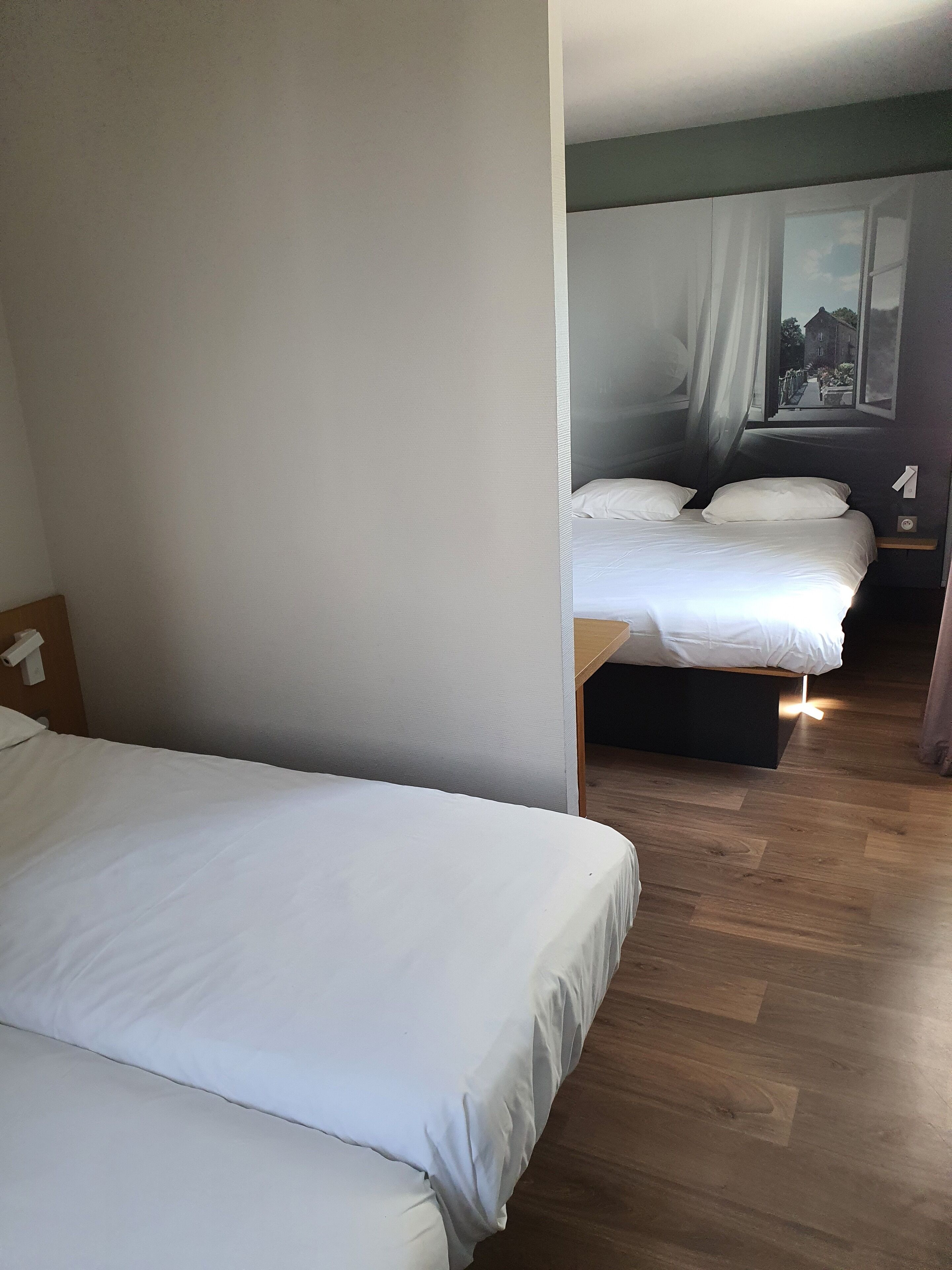 A hotel room with two beds, a wooden floor, and a view of a street through the window.