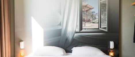 Une chambre d’hôtel avec un lit, des rideaux et une fenêtre donnant sur un espace extérieur.