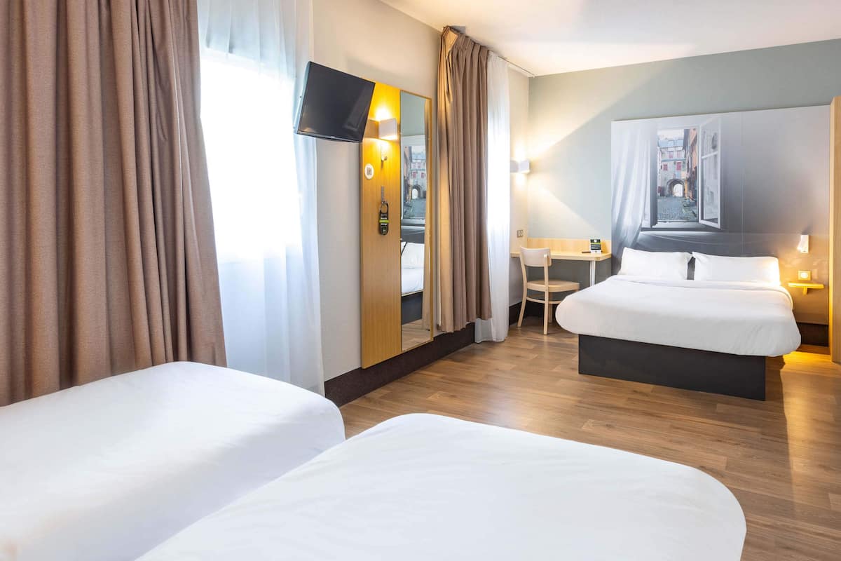 A hotel room with two beds, a desk, a chair, a TV, and a painting on the wall.
