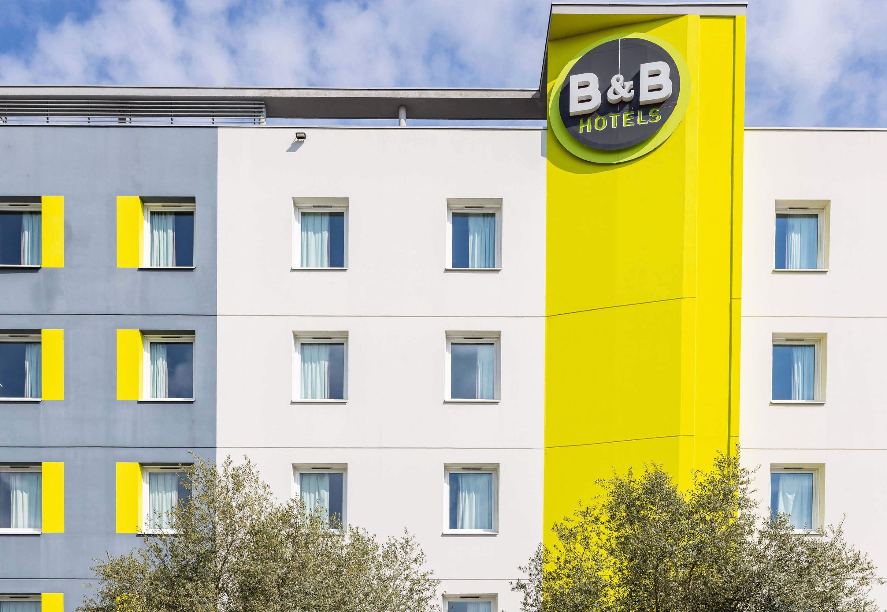 A hotel with a distinctive yellow and grey facade, featuring a prominent 'B&B Hotels' sign.
