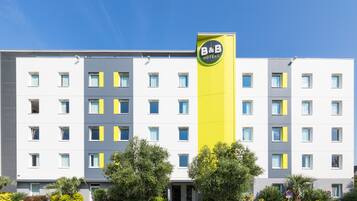 A multi-story hotel with a prominent B&B Hotels sign, featuring a modern design with a mix of white and yellow colors, and a flat roof.