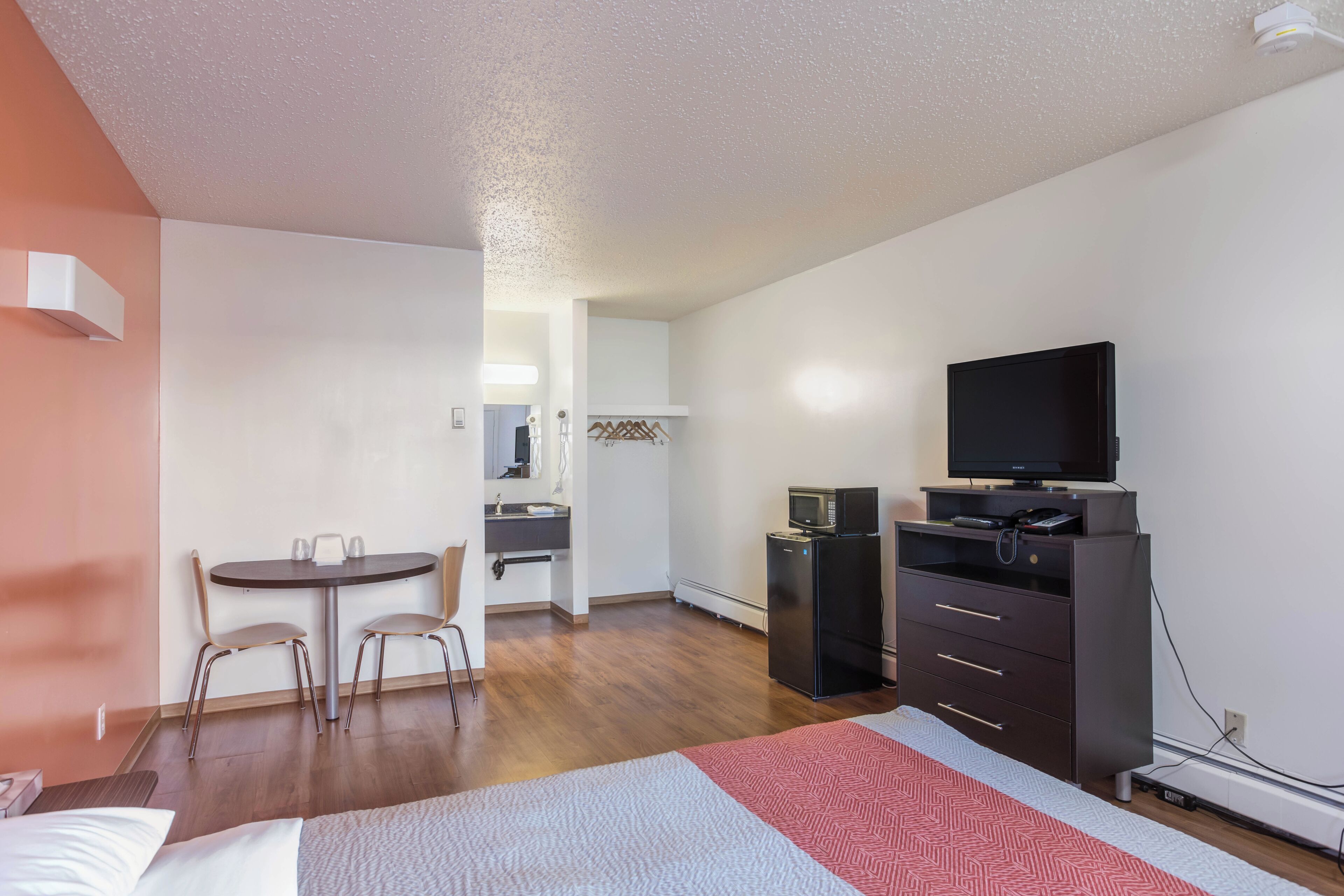 A hotel room with a bed, a desk, a chair, a television, a refrigerator, and a microwave.